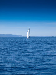 Obraz premium Front view of a sailing boat in an open blue sea and a clear blue sky