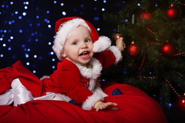 Fototapeta na wymiar Happy baby is sitting near Christmas fir-tree