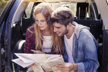 young lovers looking map sitting in the trunk of car
