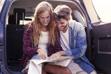 young lovers looking map sitting in the trunk of car