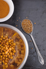 Baked spiced chickpeas in metal bowl, paprika and coriander seeds on black surface