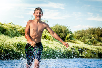 Smiling young boy running on river with copy space. Happy childhood concept.