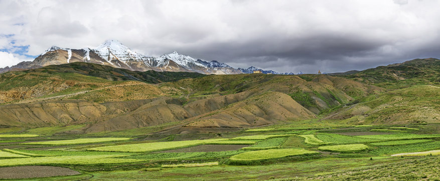 Snow mountain peaks among green fields panorama