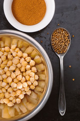 Baked spiced chickpeas in metal bowl, paprika and coriander seeds on black surface
