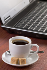 Desktop with coffee cup, opened laptop computer, diary and pen on background, no people, focused on coffee