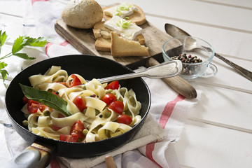 Tagliatelle Pasta with cherry tomatoes in a pan  white wooden table and red checkered tablecloth