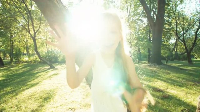 Girl running in the park at camera. Happy child in the white dress. Lens flare