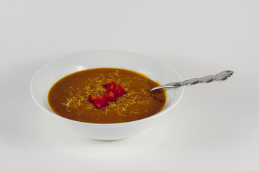 A bowl of butternut squash soup topped with a Parmesan cheese dressing and tomato garnish against a white background