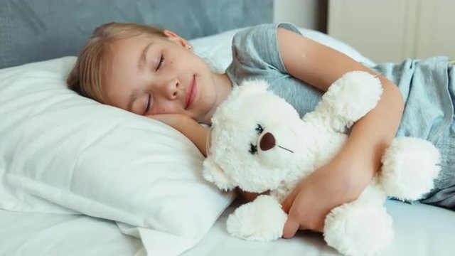 Girl sleeping and hugging teddy bear in a bed
