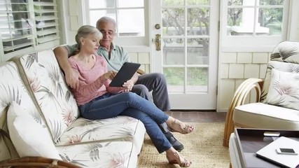 Mature couple relaxing using tablet on couch at home - Powered by Adobe