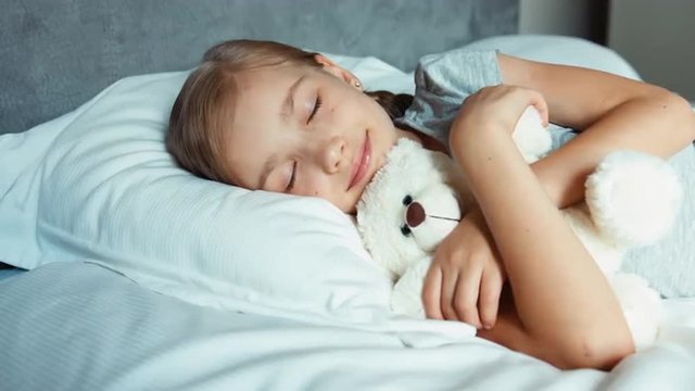 Girl sleeping in a bed with teddy bear and smiling