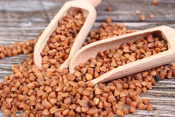 Heap of buckwheat groats with spoon on wooden surface