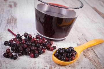 Fresh elderberry with wooden spoon and juice on old wooden background, healthy nutrition
