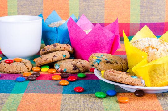 Fresh homemade muffins and cookies with color chocolate coated candies, cup of tea on a colorful checkered kitchen towel. Free space for your text