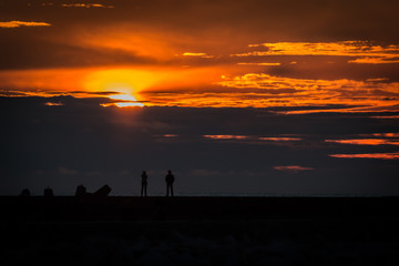 Man and woman observing sunset from a breakwater at sea