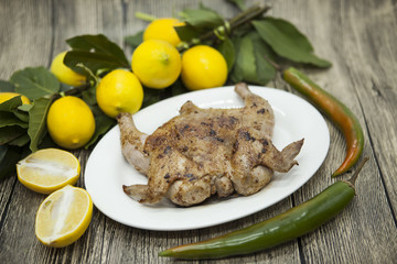Fried chicken tapaka on porcelain plate with lemon and chilli onion  on the wooden background