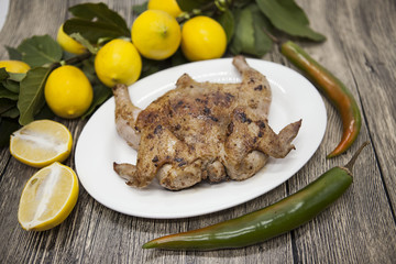Fried chicken tapaka on porcelain plate with lemon and chilli onion  on the wooden background