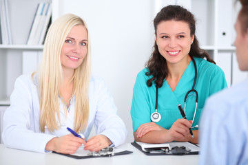 Two confident friendly female doctors sitting at the table and listen to the patient's history . Medical and health care concept