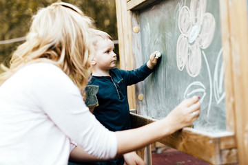Fototapeta na wymiar Beautiful mother and son drawing on blackboard with chalk