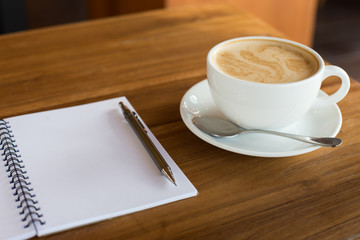 Hot latte art coffee cup on wooden table and note book, vintage