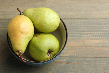 juicy green pears lying in an iron bowl on a brown wooden background