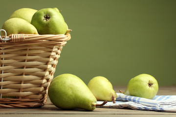 juicy green pears lay in a wicker basket  on a brown wooden table on green background