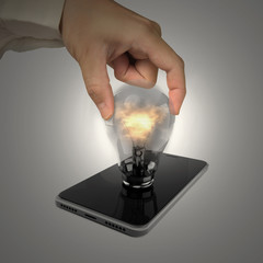 Human hand holding glowing light bulb inserted in smart phone