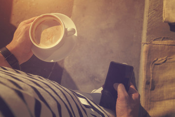 Hipster guy drinking coffee and using cellphone outdoors.