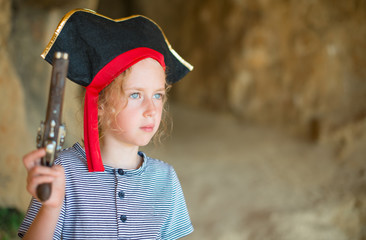 Little girl in pirate costume with musket gun near the cave entrance. Place for your text.