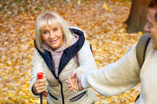 Giving a hand to a woman hiking in forest coverd by autumn leaves