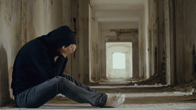 Troubled young man in wrecked abandoned building bringing his hands to his face