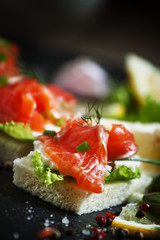Small sandwiches canapes with salty salmon,  soft cheese and gre