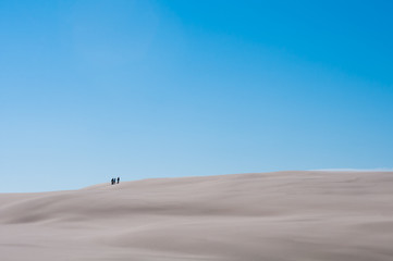 Fototapeta na wymiar Three People On Sandy Dune With Blue Sky Background