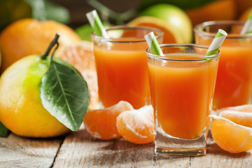 Fototapeta na wymiar Fresh juice of ripe mandarins in a small glass with striped stra