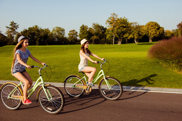 two pretty happy  girls  riding a bicycle on park