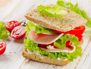 Sandwich with turkey and fresh vegetables on  a wooden table