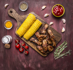 delicious roasted lamb ribs with hot sauce, on a branch with tomatoes, roasted corn, spices, on wooden rustic background top view