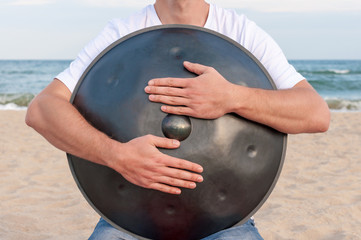 Busker hold the Hang or handpan with sea on background. The hang is a traditional ethnic drum...