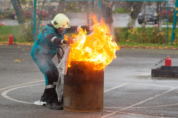 Fireman in special clothes extinguishes the fire in a barrel with a cloth