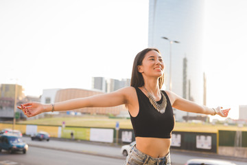 Fototapeta na wymiar Half length of young handsome asiatic long brown straight hair woman feeling free in the city with arms wide open, overlooking left, smiling - girl power, freedom, carefree concept