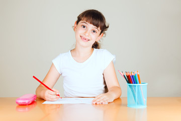 Cute little girl with red sketch pen is drawing at kindergarten