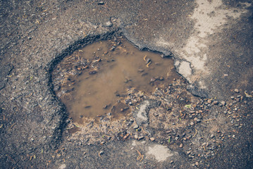 damage to tarmac road with potholes and puddles