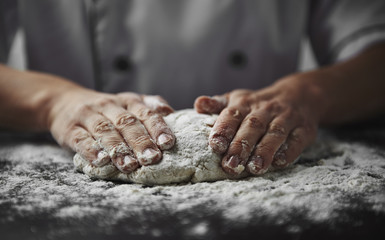 Close-up of woman baker hands kneading the dough on black board with flour powder. Concept of baking and patisserie.    - obrazy, fototapety, plakaty