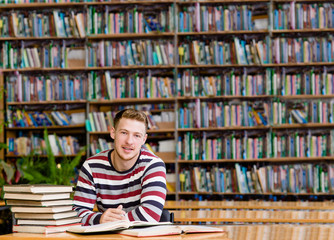 Smiling male student with open book working in a library