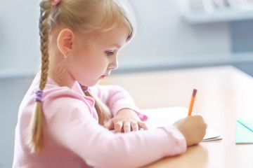  five years old  blonde girl sitting at classroom and writing