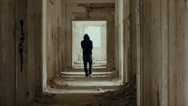 Hooded,troubled young man in wrecked abandoned building walking away