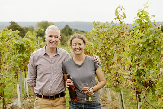 A couple, vineyard founder and her partner standing among the rows of vines. 