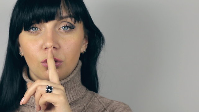 Brunette girl puts finger to her mouth, urging silent