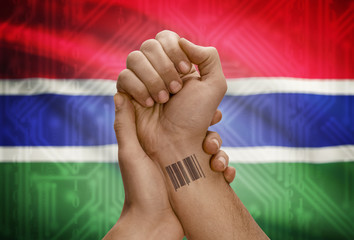 Barcode ID number on wrist of dark skinned person and national flag on background - Gambia