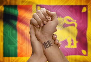 Barcode ID number on wrist of dark skinned person and national flag on background - Sri Lanka